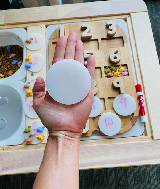 A large acrylic coin sits on a hand above a wooden board