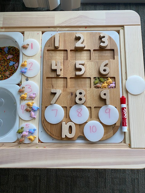 A set of acrylic coins sits on a wooden learning board for sensory bins